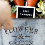 Easter bunny centerpiece with faux carrots, spring florals, and a 'Free Carrots' sign in a rustic garden bucket.