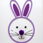Easy DIY Easter bunny craft using a toilet paper roll as a stamp to create a bunny face with purple ears, googly eyes, and a pom-pom nose.