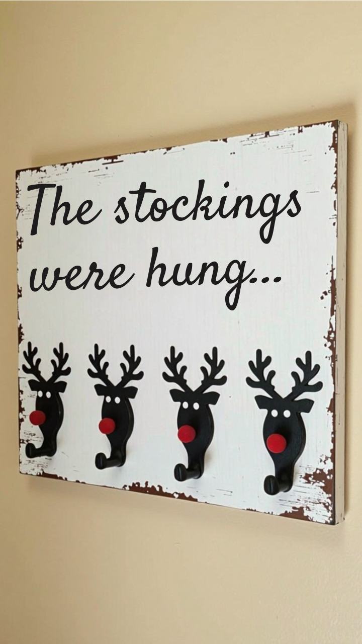 Rustic Christmas stocking holder with black reindeer hooks and red noses on a distressed wood sign reading “The stockings were hung." 
