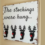 Rustic Christmas stocking holder with black reindeer hooks and red noses on a distressed wood sign reading “The stockings were hung."