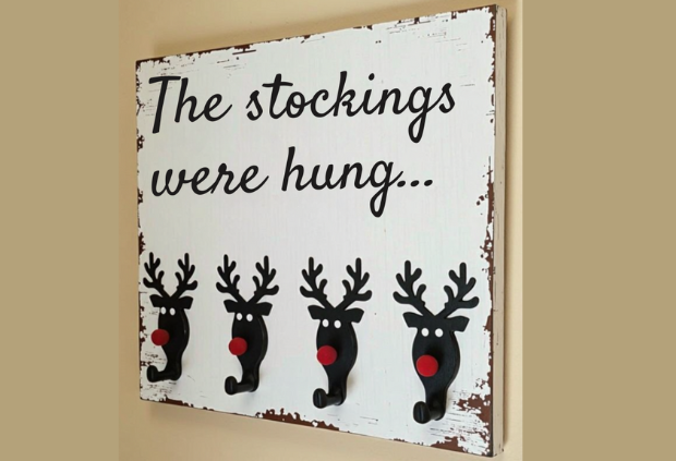 Rustic Christmas stocking holder with black reindeer hooks and red noses on a distressed wood sign reading “The stockings were hung."