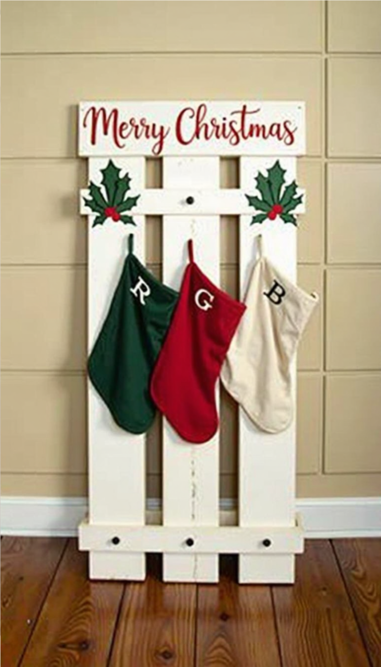 DIY Christmas stocking holder made from a white picket fence with holly decorations and three hanging stockings with initials.