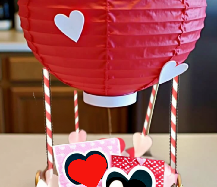 DIY Valentine's Day hot air balloon basket made from a wicker basket and red paper lantern, decorated with white hearts and filled with Valentine's gifts