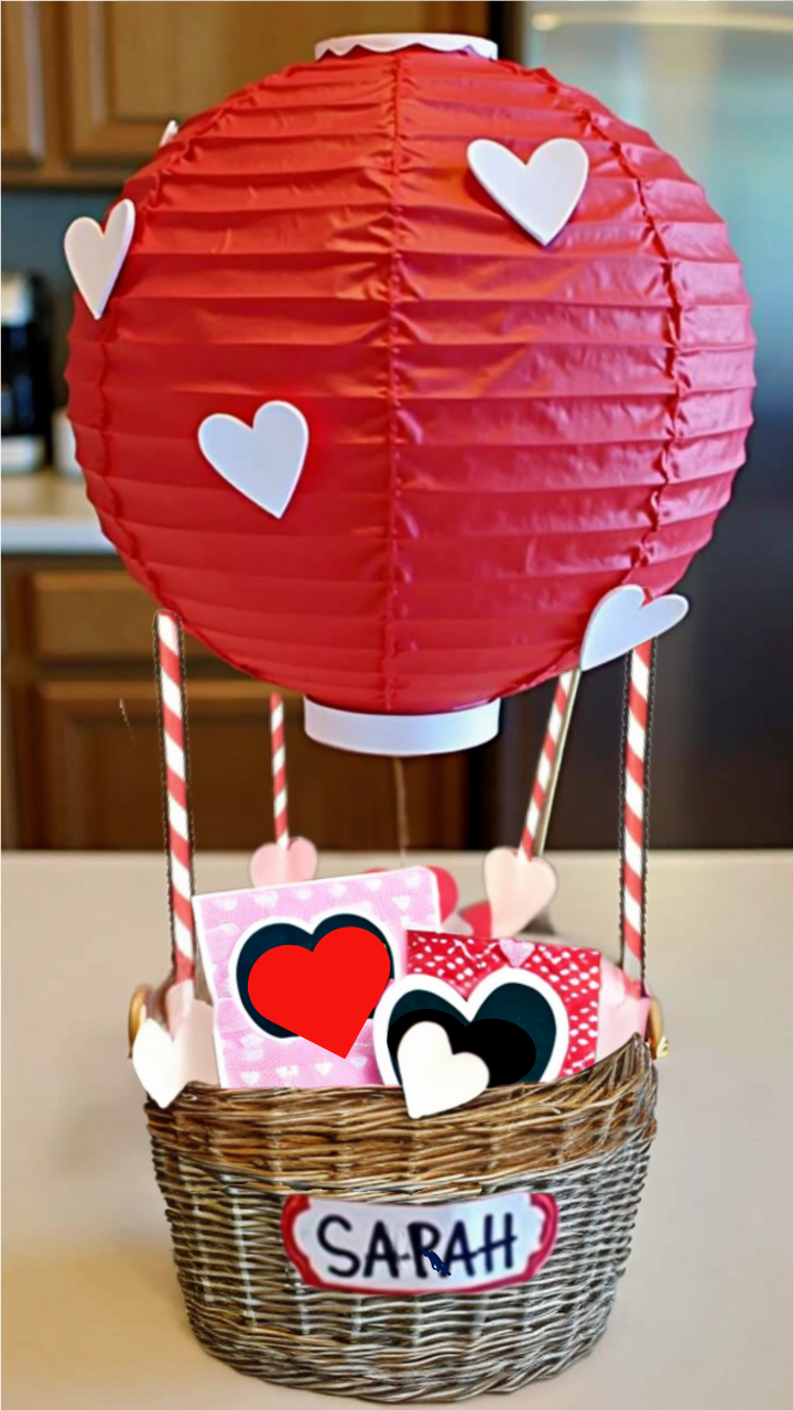 DIY Valentine's Day hot air balloon basket made from a wicker basket and red paper lantern, decorated with white hearts and filled with Valentine's gifts