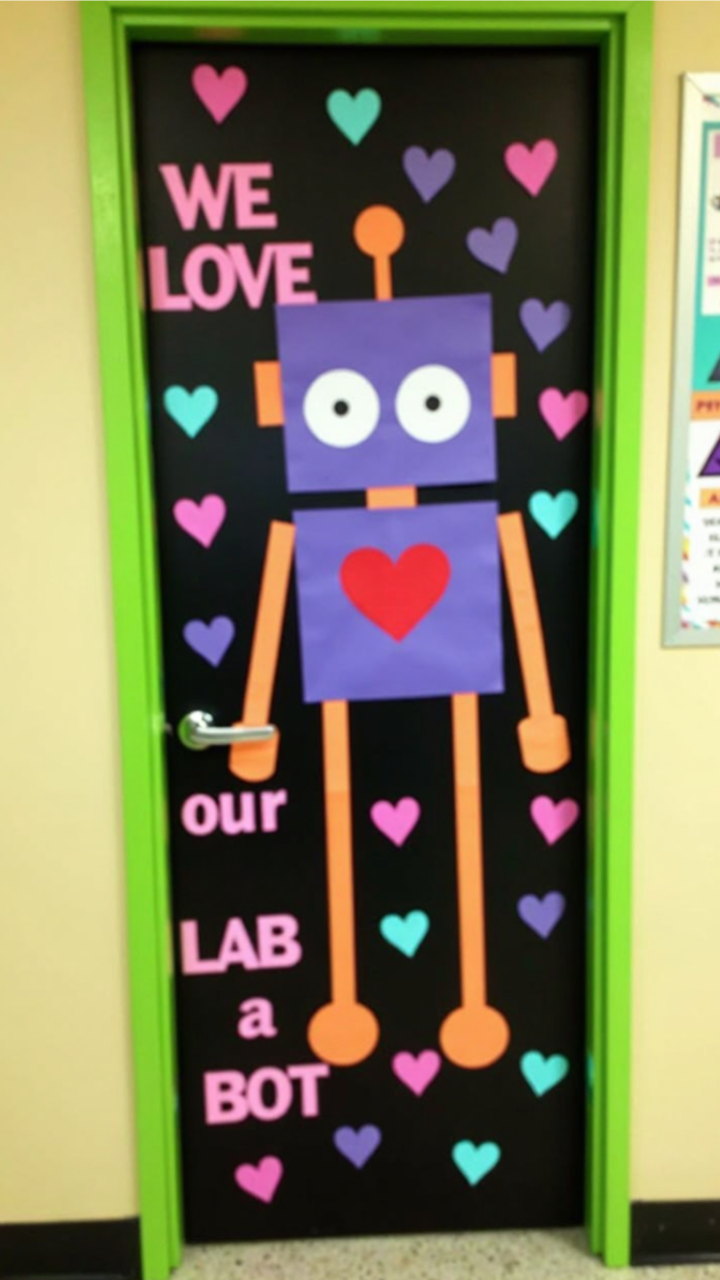 Classroom door decorated with a Valentine's Day theme, featuring a large robot made of paper with a heart on its chest, surrounded by colorful hearts and the phrase 'We love our lab a bot.